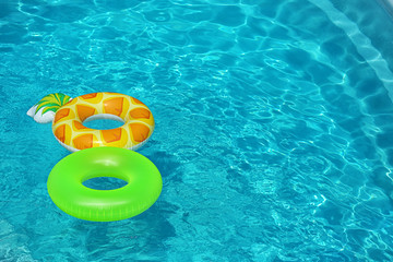 Bright inflatable rings floating in swimming pool on sunny day. Space for text