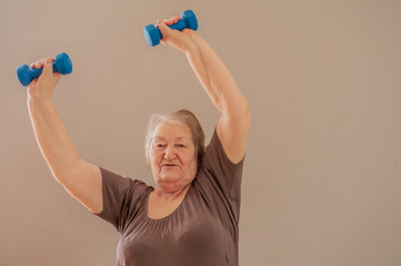  Health-conscious. Charming upbeat elderly lady working out with dumbbells and smiling pleasantly at the camera at home.