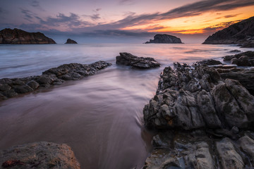 Colorful cloudy Sunrise at the beach of playa de la arnia with dynamic waves and bizarre rocks, Liencres, Northern Spain