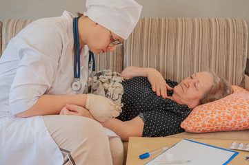 Pretty nurse in white coat helps sick retiree on social assistance program. Nurse carefully examines prescription of drugs, makes injections, measures blood pressure and cares.
