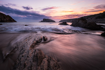 Colorful cloudy Sunrise at the beach of playa de la arnia with dynamic waves and bizarre rocks, liencres, Northern
