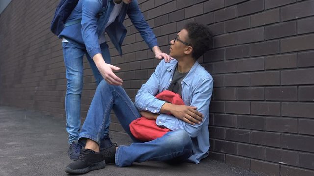 Teenage student giving helping hand to bullied afro-american boy, stop racism