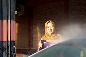 portrait of happy hijab women car cleaning - Removing the soap with water, using a garden hose and a spray gun.