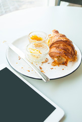 Fresh crispy croissant with jam, butter and cappuccino with beautiful latte art on grey table in a cafe.