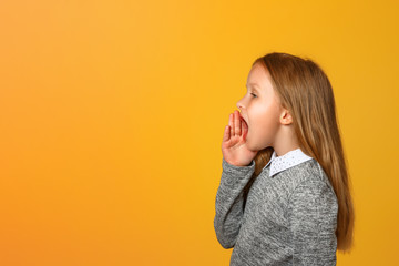 The little girl screams loudly to the side with a hand over her mouth. Close-up. Yellow background....