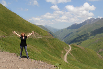 woman in black clothes, a tourist stands, having stretched her arms in beautiful alpine meadows, green mountains of Georgia, Bear Cross Pass, 2700 meters