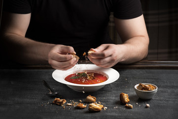 Summer fresh healthy, spicy, cold, tomato gazpacho soup with basil bread and onions, served on a dark table. . Mens hands with bread over a plate, Spanish cuisine.
