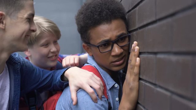 Cruel teenagers pushing black boy to wall, racial hate and bullying in schools