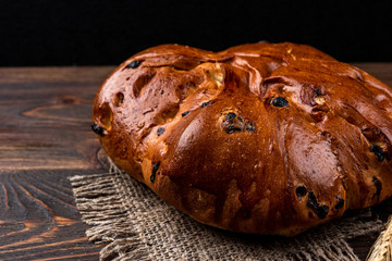 Bun with raisins on dark wooden background.