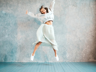 Fototapeta na wymiar Beautiful cute smiling model jumping. Girl in summer hipster hoodie and skirt. Model having fun and going crazy near gray wall in studio