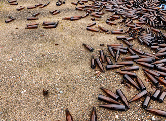 whole and broken brown bottles are scattered on gravel.Concept: waste recycling, disposal of garbage