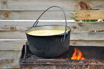Millet porridge in a pot on the grill with fire, on the wooden fence background