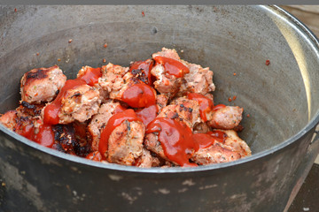 Pork meat from the grill with ketchup in a metal pot on the grill, against a wooden fence