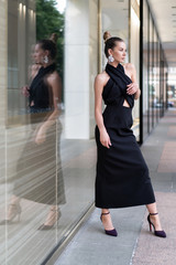 European model originally posing in a black dress near the boutique. In the glass you can see its reflection. Very stylish interesting atmosphere for advertising fashion trends.