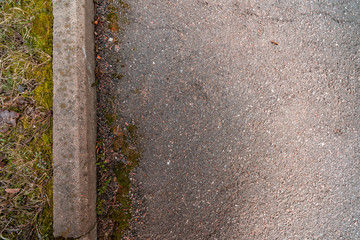 Dark worn asphalt with curb and old moss