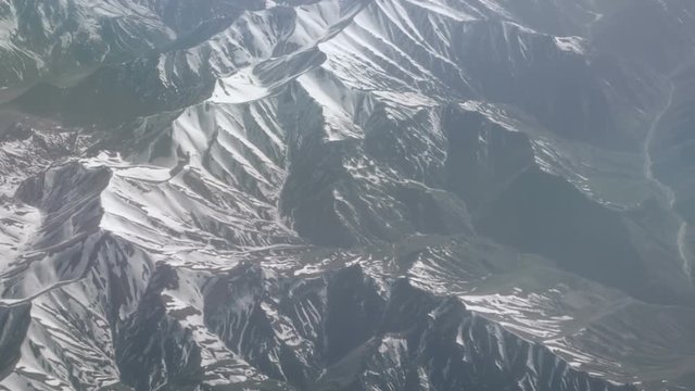 Aerial view of snowy mountains. View from the plane on a mountain folds. The tops of the mountains covered with snow view from the window of the plane. Alborz or Alburz, Elburz or Elborz