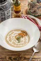 A plate of delicious homemade mushroom cream soup with onion rings on top on wooden table