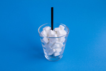 Glass with sugar cubes on the blue background.Copy space.Unhealthy food concept.