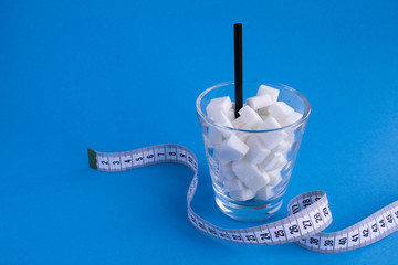 Glass with sugar cubes  and white centimeter on the blue background.Copy space.Unhealthy food concept.