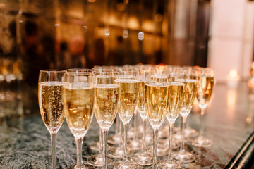 Close-up of glasses of champagne in a row on a table. A lot of wine glasses with a cool delicious champagne at the restaurant. Bubbles view from the side close-up.