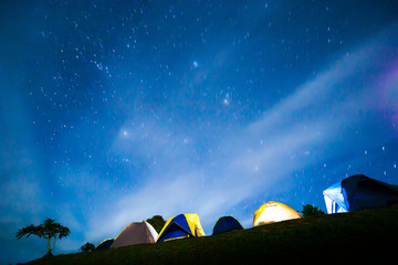 Illuminated camping tents under starry night sky.