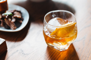 Single malt Scotch whisky in drinking glass with sphere ice and orange peel on wooden table.