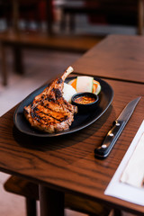 Thai style BBQ Pork chop served with sticky rice, sliced carrot and Thai spicy sauce. Served in black plate with knife on wooden table.
