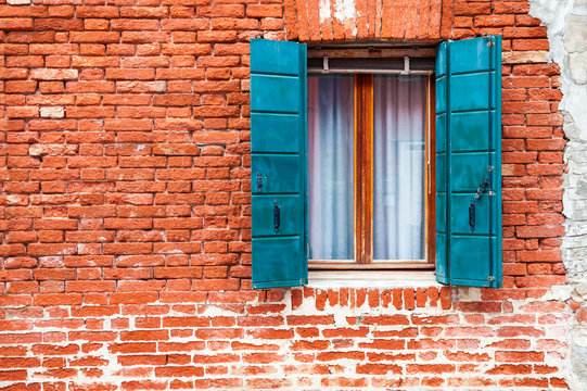 Window with blue shutters on the old red brick wall. Burano island, Venice, Italy.