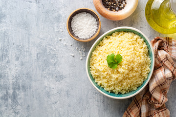 Cooked couscous with cilantro in ceramic bowl on concrete background. Top view. Copy space.