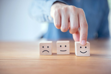 Close up customer hand choose smiley face and blurred sad face icon on wood cube, Service rating,...