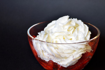 Strawberries with whipped cream in a transparent bowl on a dark background