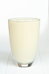 A large transparent glass is filled with a cold summer drink made from vegetable milk and a filler on a white wooden table with an isolated background, photo for the menu