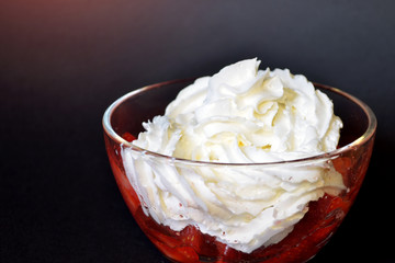 Strawberries with whipped cream in a transparent bowl on a dark background with a red glow