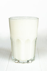 A large transparent glass is filled with a cold summer drink made from vegetable milk and a filler on a white wooden table with an isolated background, photo for the menu