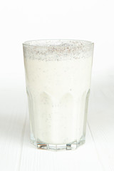 A large transparent glass is filled with a cold summer drink made from vegetable milk and a filler on a white wooden table with an isolated background, photo for the menu