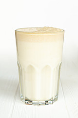 A large transparent glass is filled with a cold summer drink made from vegetable milk and a filler on a white wooden table with an isolated background, photo for the menu