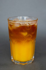 A large transparent glass filled with cold summer drink with ice cubes is photographed on a gray, isolated background, photo for the menu.