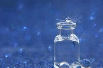 Dandelion seed with drop of water in glass bottle on blue bokeh background. An artistic picture of dandelion flower.