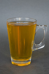 a transparent mug with a handle filled with hot bright tea of intense color on a dark gray background, the photo is suitable for the menu of cold tea in the cafe
