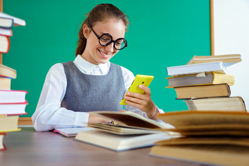 Happy girl looks at the phone and reads the message. Photo of student in uniform, wearing glasses. Education concept