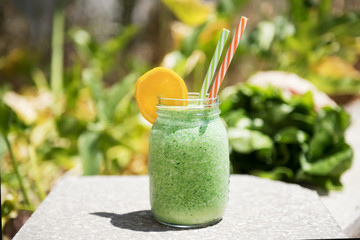 Summer healthy detox drink: blended green smoothie in a city park or garden in the bright midday sun