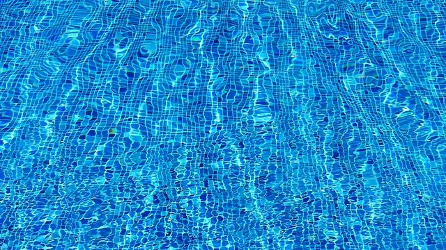 Water texture. The reflection of the rays of the sun in the clear water of the blue pool.