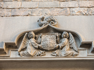 Two angels hold an ancient shield of Barcelona, which contains Masonic symbols, on a dragon. Door of the Convent of San Agustín.
