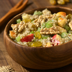 Quinoa Waldorf Salad with apple, celery, yellow raisins and walnut served in wooden bowl, photographed on dark wood with natural light (Selective Focus, Focus one third into the salad)