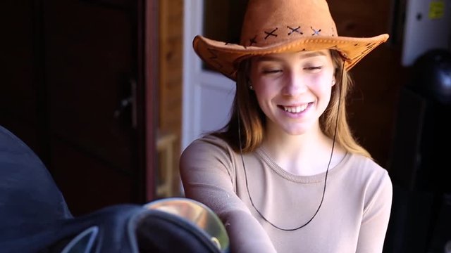 The girl wears a saddle on a horse in a cowboy hat