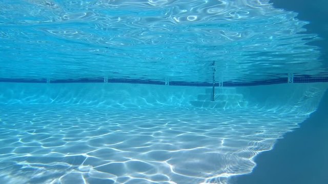 Clean empty suburban swimming pool with underwater sunlight movement.