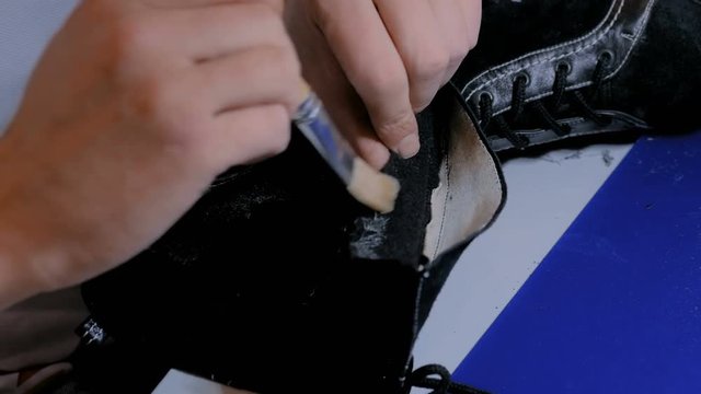 Professional man shoemaker, cobbler holding brush with glue and repairing black female boot at workshop, studio. Design, handmade, restoring and shoe repair concept