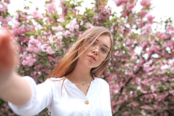 beautiful young happy woman in a blouse and glasses near the cherry blossoms. flowers