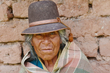 Old native american woman wearing typical aymara clothes. Adobe wall background.