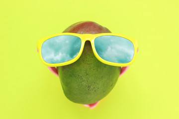 Ripe juicy green and red mango in sunglasses on pastel yellow background.Copy space. minimalistic style.